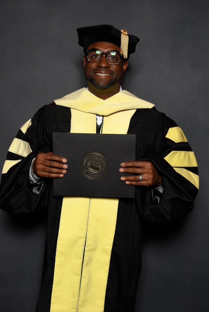 Dr. Shawn C. Brown in doctoral regalia holding his diploma cover